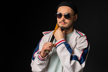 A young, tough guy from the streets dressed in a tracksuit and round sunglasses holding a baseball...