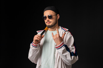 A young, tough guy from the streets dressed in a tracksuit and round sunglasses holding a baseball...