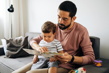 Happy father and toddler son reading book at home - Powered by Adobe