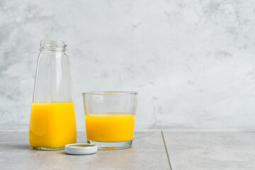 Bottle and glass with yellow liquid juice halthy beverage on gray concrete background. Orange fresh