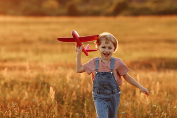 The girl runs across the summer field and launches a toy plane into the sky. A child plays aviator or pilot in a field at sunset, a happy childhood. © Kaplitskaya Love