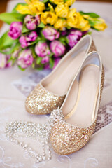 Fototapeta na wymiar Shoes with gold glitter against a backdrop of yellow and pink tulips along with beads