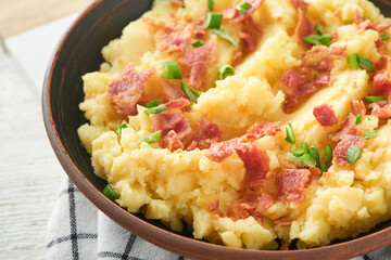 Mashed boiled potatoes. Bacon mashed potatoes with green onion, pepper and cheddar cheese in bowl on light old wooden backgrounds. Delicious creamy mashed potatoes. Top view.