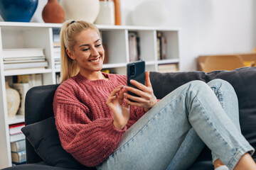 Obraz premium young adult caucasian woman sit on sofa and using smartphone