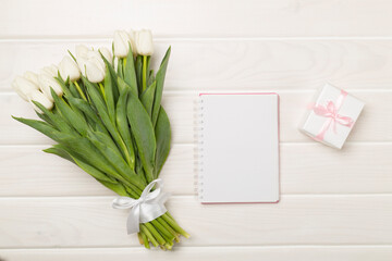 White tulip bouquet with notebook on wooden background, top view