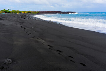 Footprints on Black Sand Along the Ocean Coastline