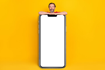 Photo of funky positive guy pensioner dressed red t-shirt holding modern gadget empty space isolated yellow color background