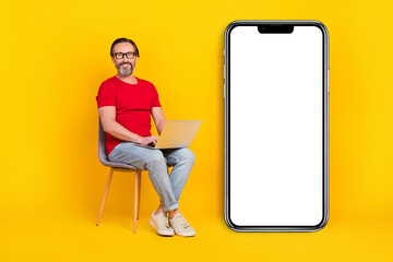 Photo of cute cheerful guy pensioner dressed red t-shirt glasses writing gadget empty space isolated yellow color background