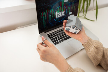 woman holding a toy house with a laptop and taxes