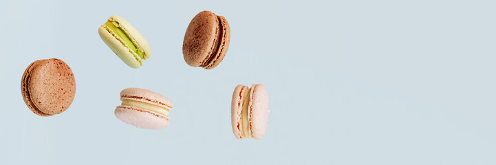 Lots of macarons falling down isolated on blue background. Background for the confectionery menu....