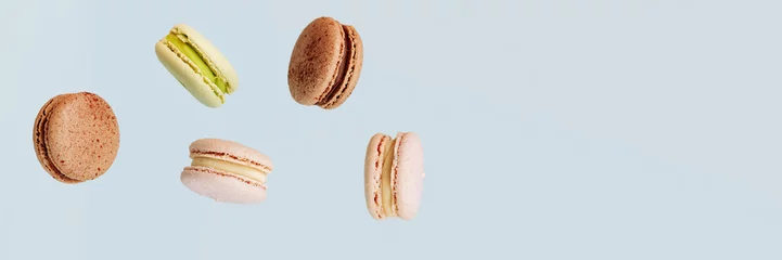 Keuken foto achterwand Macarons Lots of macarons falling down isolated on blue background. Background for the confectionery menu. Banner for website header design with copy space.