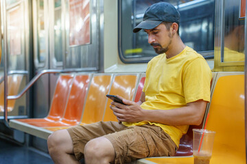 Young man sitting in New York City subway train texting and using a phone reading his correspondence