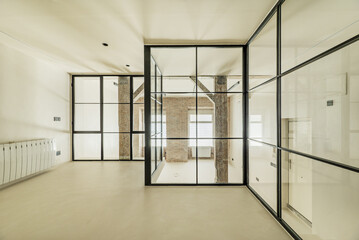 Loft-style room with glass partitions and black metal frame, plain beige walls and floors, and old wooden pillars