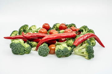 Red hot chili peppers, ripe cherry tomatoes and raw broccoli stalks on a plain white surface