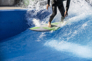 A surfer dressed in his black neoprene suit raising foam in the waves of a swimming pool