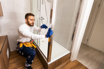 The worker is connecting the glass walls of the shower enclosure with a metal bar.