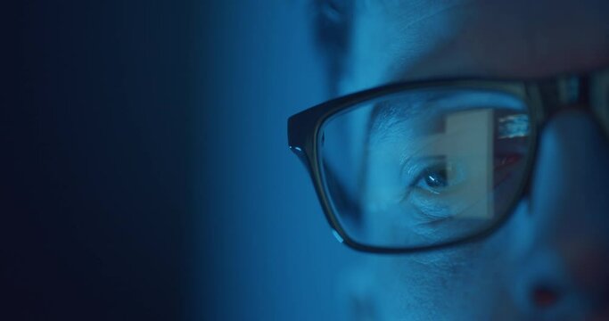 Reflection of scrolling on laptop screen in man's glasses at night