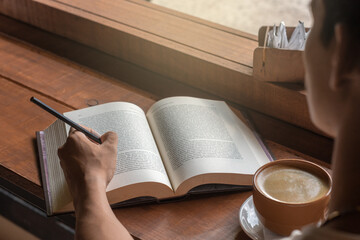 Latín man holding a cup of Coffe and reading a book in a café by the window after getting up in the morning. Morning lifestyle concept.