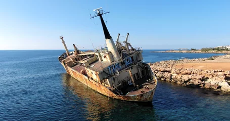 Foto op Canvas Flying drone over the coastline of the island overlooking an old rusty sunken ship or liner, rocky shoreline with vegetation and rocks and clear sea with light foamy waves in Cyprus. © Anton
