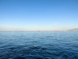 Calm seascape with blue calm sea waves in İzmir, Konak, Türkiye. View of Mediterranean Sea from coast with ships and mountain silhouette background.