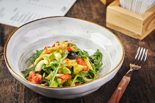 Salad with squid, arugula, celery and avocado, tomatoes and olives on white plate on wooden table