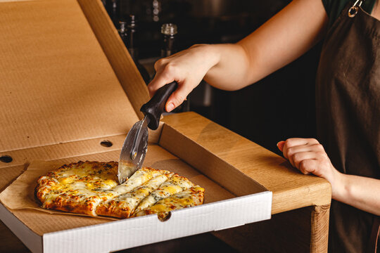 Woman's hand cuts pizza in box with roller knife. Roman square pizza or Pinsa on thick dough, Italian Cuisine