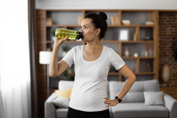 Multiethnic young woman in sportswear drinking water during training at home. Female athlete...