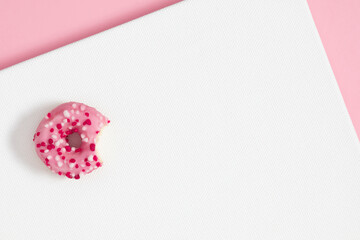 White empty canvas and bitten pink donut. Flat lay, top view, copy space