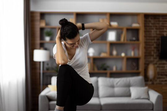 Strong multicultural young woman wearing sport clothes doing knee to elbow crunches at cozy living room with modern interior. Concept of people and healthy lifestyles.