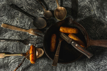 Still life in a rustic style- fried sausages in a cast-iron pan on a dark background