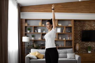 Focused african woman in sport clothes doing fitness exercises with hands during workout at home. Active young brunette enjoying morning training for staying fit and healthy.