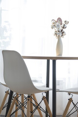 A bouquet of cotton twigs in a vase on a round table with an Easter decor of eggs and an Easter bunny in the light from the window in a minimalist interior.