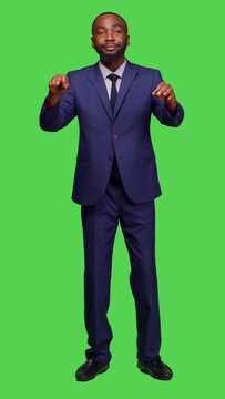 Vertical video: Front view of african american man having choir concert for opera event, conducting symphony standing over greenscreen backdrop. Male musician choirmaster playing formal music, modern