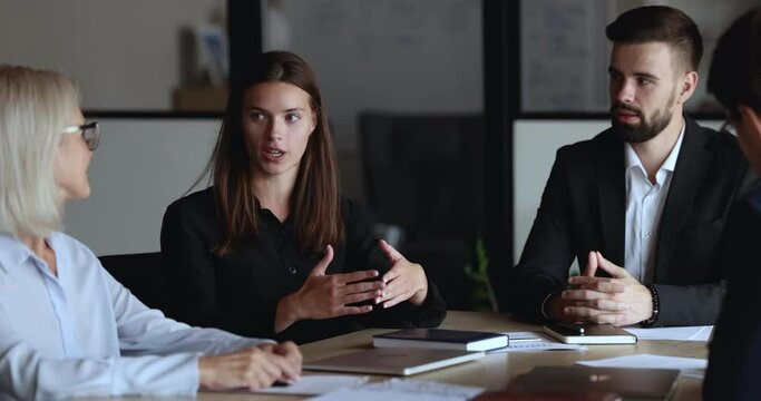 Young millennial team leader, businesslady, executive manager leads formal meeting with partners, entrepreneurs gathered in board room, make speech, take part in negotiation, talk about work results