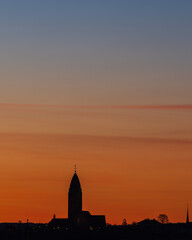 The majestic Masthugget Church stands silhouetted against a vivid orange sky at dawn, its stunning architecture the perfect backdrop to Gothenburgs skyline.