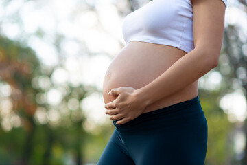 Pregnant woman in uniform sportswear blue top, leggings. Holding, touching belly on blurred background. Skin care concept.