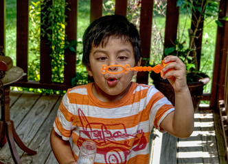 Mexican boy blowing bubbles outside on a porch