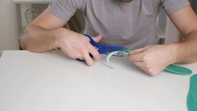 A man cuts out new shoe insoles with scissors to fit his foot size.