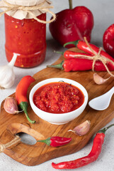 Traditional sauce adjika with hot chili pepper, paste harissa in white bowl on wooden board
