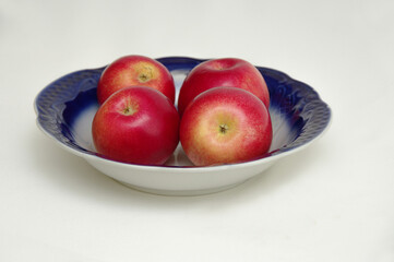 Red apples in a blue plate on a white background with a shadow. Close-up. Selective focus.