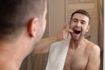 Man opening his mouth in the mirror to observe his dental health 