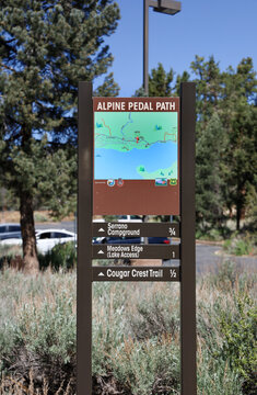The Alpine Pedal Path sign with map with route. Serrano Campground, Meadow Edge (Lake Access) and Cougar Crest Trail sign at the Discovery Center in Fawnskin, California - USA -on May 22, 2022.