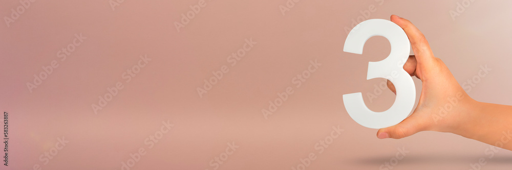 Aufkleber number three in hand. hand holding white number 3 on red background with copy space. concept with nu