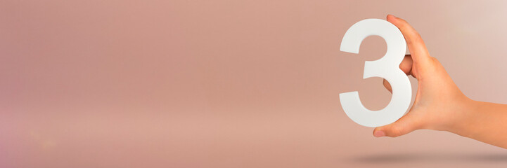 Number three in hand. Hand holding white number 3 on red background with copy space. Concept with...
