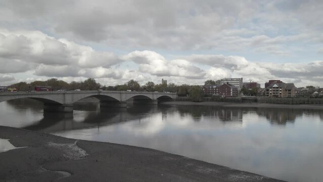 Calm River Thames flowing under Putney Bridge connecting Putney and Fulham borough in West London. Vehicles driving on road. London, UK