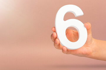 Number six in hand. A hand holds a white number 6 on a red background with copy space. Concept with...