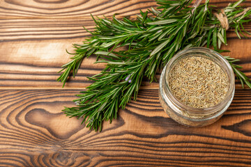 Dried rosemary in a glass jar, branches of fresh rosemary on a brown wooden background.Spices and herbs for meat and fish.Recipe.Culinary concept.Organic herbs. Place for text.