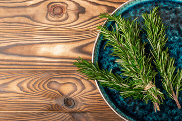 Fresh rosemary herb in a blue plate on a brown wood.Bunch of fresh fragrant rosemary. Spices and herbs for meat and fish. Recipe. Culinary concept.Organic herbs.Place for text. Space for copy. 