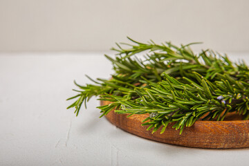 Fresh rosemary herb in a wooden plate on a white wood.Bunch of fresh fragrant rosemary. Spices and herbs for meat and fish. Recipe. Culinary concept.Organic herbs.Place for text. Space for copy. 
