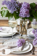 Beautiful table decor for a wedding dinner with a spring blooming lilac flowers. Celebration of a special holiday marriage event. Fancy white plates, wineglasses. Countryside style